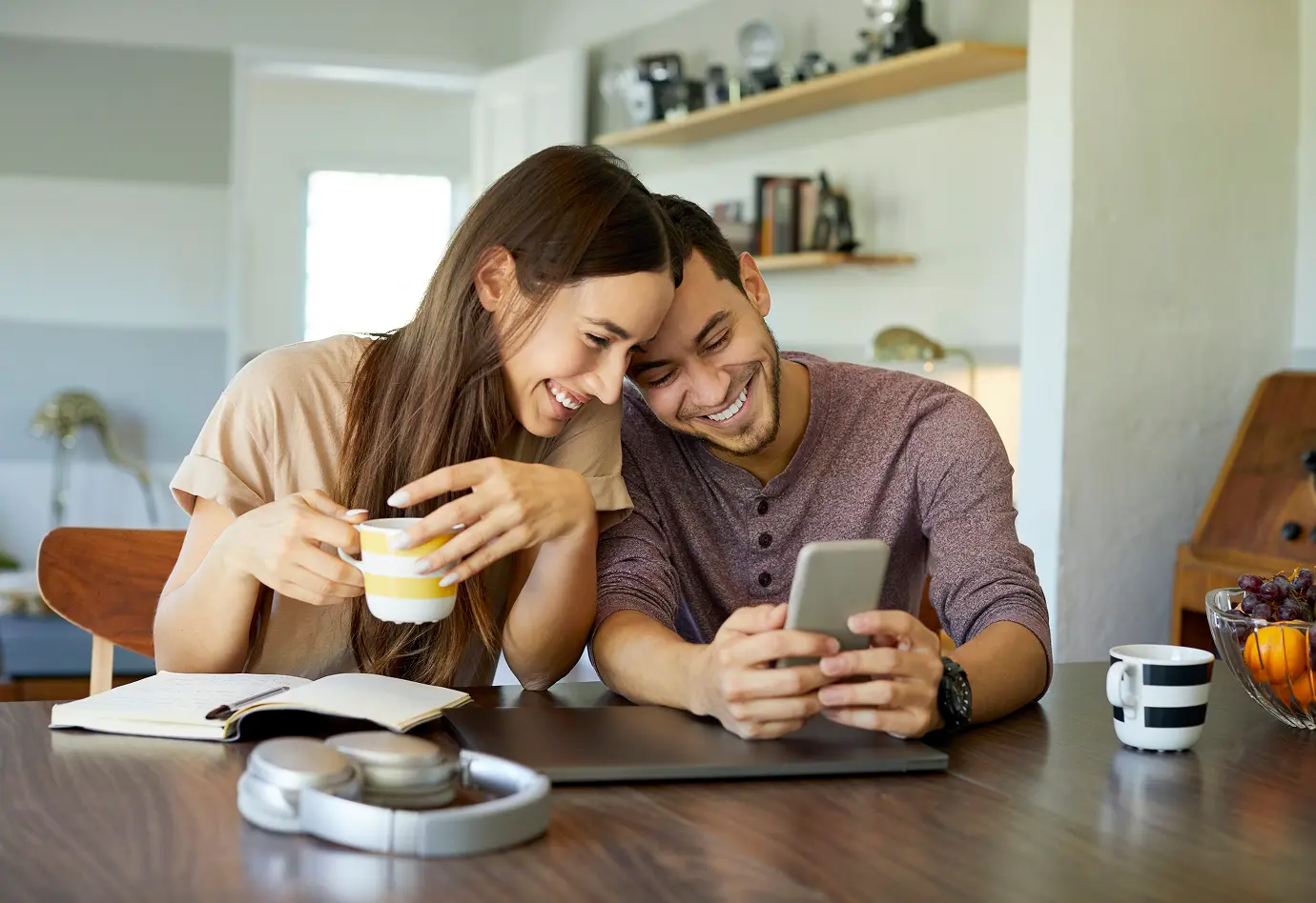 Couple sitting at table smiling and looking at a phone together.